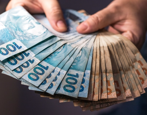 Mão segurando notas de 100 Reais Brasileiros